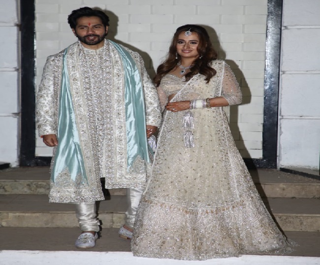 वरुण धवन और नताशा दलाल बैठे हुए हैं और परिवार फूलों से कर रहा है वर्षा
