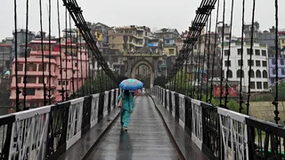 शुक्रवार को मंडी में बारिश के बाद लोग छतरी का सहारा लेकर विक्टोरिया पुल से गुजरते हुए। (एएनआई फोटो)