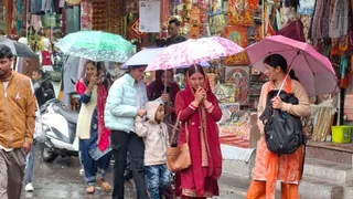 देहरादून में बारिश के बीच छाता लेकर जाती महिलाएं।