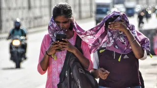 तेज धूप से बचने को सिर ढककर गुजरती युवतियां।