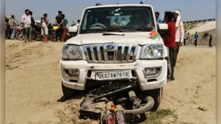हादसे के बाद खेत पर खड़ी सपा का झंडा लगी कार और उसके नीचे फंसी बाइक। जागरण