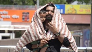 प्रयागराज में चिलचिलाती घूप में अपने बच्चे को बचाने के लिए तैलिया में लपेटक ले जाता पिता। जागरण