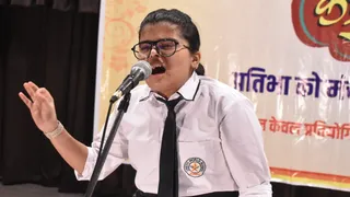 धनबाद में बाल कवि सम्मेलन 2026 में काव्य पाठ करतीं छात्रा। (फोटोः जागरण)