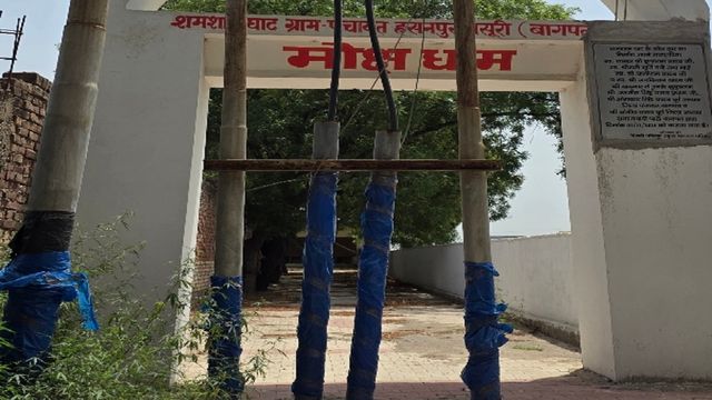 बागपत में पावर कारपोरेशन ने लापरवाही की हद कर दी! श्मशान घाट के गेट के बीचों-बीच लगवा दिए बिजली के खंभे
