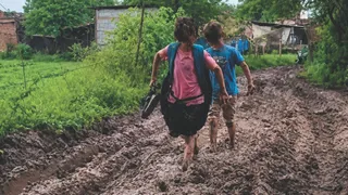 हाथ में जूते लेकर रास्ता पार करते हुए बच्चे
