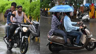 बारिश के बीच वाहन से निकलते लोग