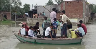 गांव आशा की मड़ैया में भरे बाढ़ के पानी में नाव से घर जाते स्कूल के बच्चे। जागरण
