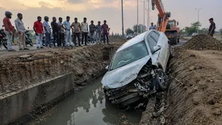 तेज रफ्तार कार एक बाइक सवार को बचाने के प्रयास में अनियंत्रित होकर सड़क किनारे निर्माणाधीन नाले में जा गिरी। एआई इमेज