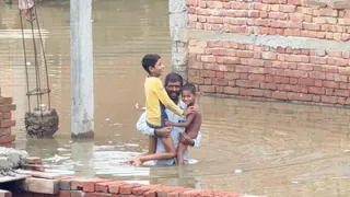 गजरौला के मुहल्ला मायापुरी में वर्षा से हुआ जल भराव बच्चो को गोद में लेकर निकलते स्वजन। जागरण