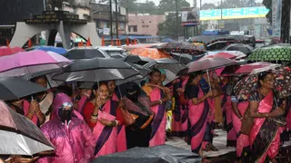 धनबाद के रणधीर वर्मा चाैक पर झमाझम बारिश के बीच छाता लेकर प्रदर्शन करतीं आंगनबाड़ी सेविकाएं। (फोटोः अमित सिन्हा)
