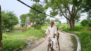 मुबारिकपुर में मुख्य सड़क के किनारे स्थित पेड़ से बांधा गया हाईटेंशन विद्युत लाइन का केबल और नीचे से गुजरता साइकिल सवार l जागरण