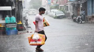प्रयागराज में वर्षा के बीच सामान लेकर जाता युवक। जागरण