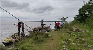 नदी किनारे गांव के लोग नाव द्वारा नदी से निकाल रहे लकड़ियां