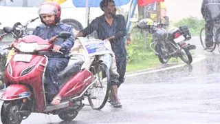 बारिश के बीच मुश्किलों का सफर: तेज बारिश के दौरान स्कूटी से जाती महिला और साइकिल ले जाता आदमी। (फोटो जागरण)