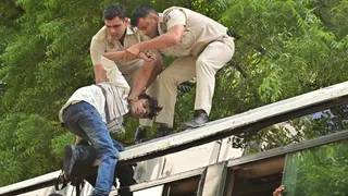 अशोक रोड पर बस पर चढ़कर प्रदर्शन कर रहे एक प्रदर्शनकारी को हिरासत में लेते पुलिसकर्मी। जागरण