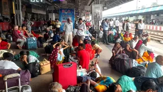 ट्रेन के इंतजार में स्टेशन पर बैठे यात्री।