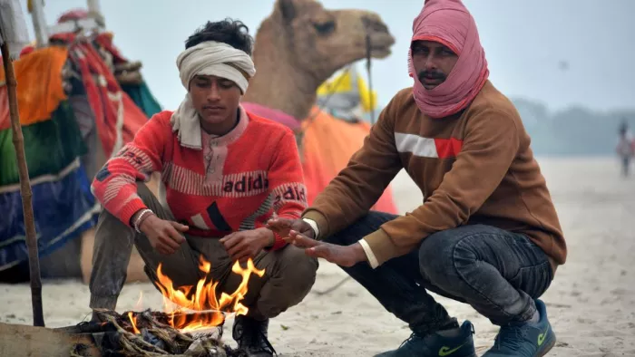 UP Weather News ठंड से बचने के लिए वाराणसी में गंगा उसपार रेत पर ऊंट चालक आग तापते। जागरण