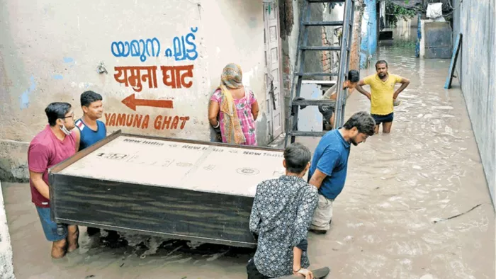 यमुना बाजार क्षेत्र में भरे पानी के बीच सामान सुरक्षित स्थान पर ले जाते लोग। ध्रुव कुमार