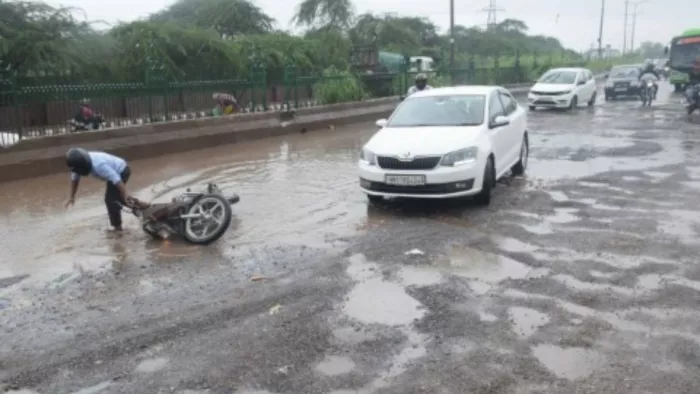ओखला लैंडफिल साइट के सामने टूटी सड़क पर पानी भरे गड्ढों में फंसकर गिरा बाइक सवार
