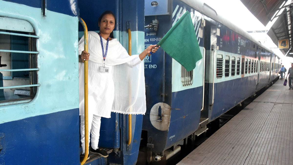 A realistic Indian female train loco pilot in uniform, standing near a railway engine looking concerned or distressed, empty railway station background, monsoon sky, subtle highlight on her expression, no toilet around, emphasis on loneliness and struggle, photojournalism style, cinematic lighting, 16:9 aspect ratio, high resolution.
Text on image: "इंजन में नहीं है वॉशरूम!"