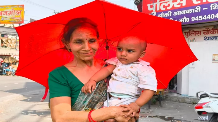 Weather Update: गर्मी में बच्चे को छाता की छांव में लेकर जाती महिला।