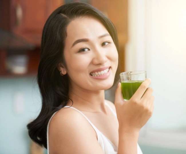 ग्लास में हरे रंग का काढ़ा पीती हुई युवती
