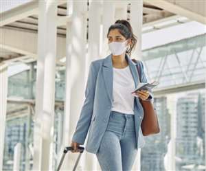 मास्क लगाए ब्लू सूट में हाथ में मोबाइल, हैंडबैग लिए हुए महिला