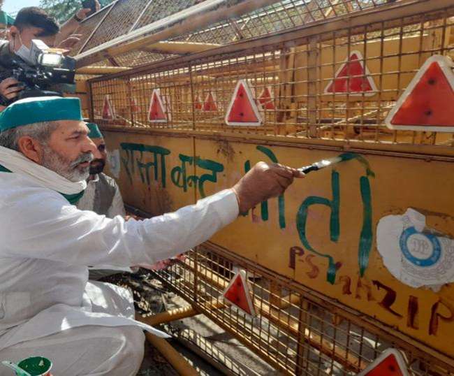 राकेश टिकैत हरे रंग से यहां लगे बैरिकेड पर लिखते हुए।