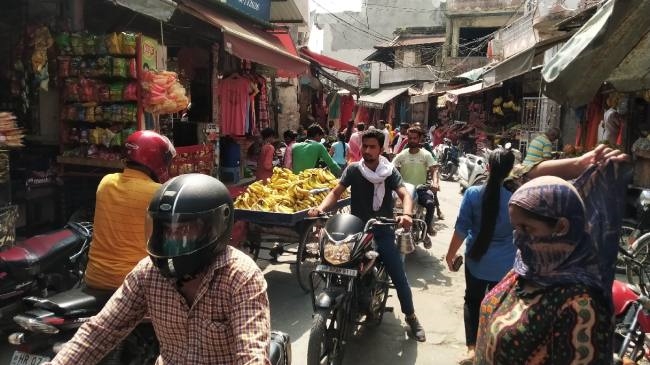 बाजार में बेचने को मास्क, चेहरे खुले हुए