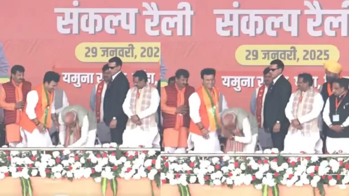 Delhi Election 2025: पीएम मोदी ने मंच पर बीजेपी प्रत्याशी रविंद्र सिंह नेगी के पैर छुए। फोटो - पीटीआई